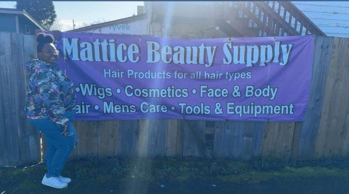 Champaine McNair, the new owner of Mattice Beauty Supply, poses in front of the store’s sign.
