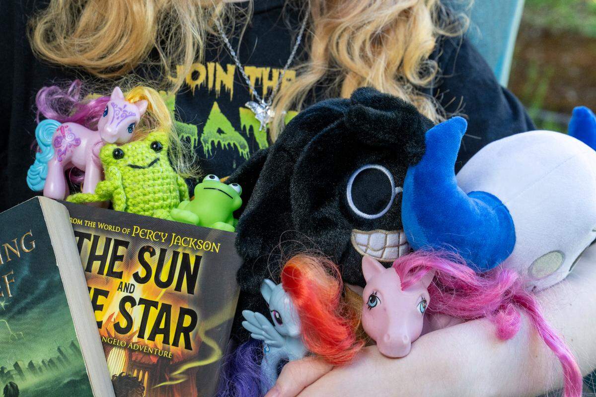 Phoebe holds favorite items from their home, including books from the Percy Jackson series, My Little Pony characters, frogs and stuffed characters from Roblox games, on Thursday, May 1, 2025, in Tacoma.