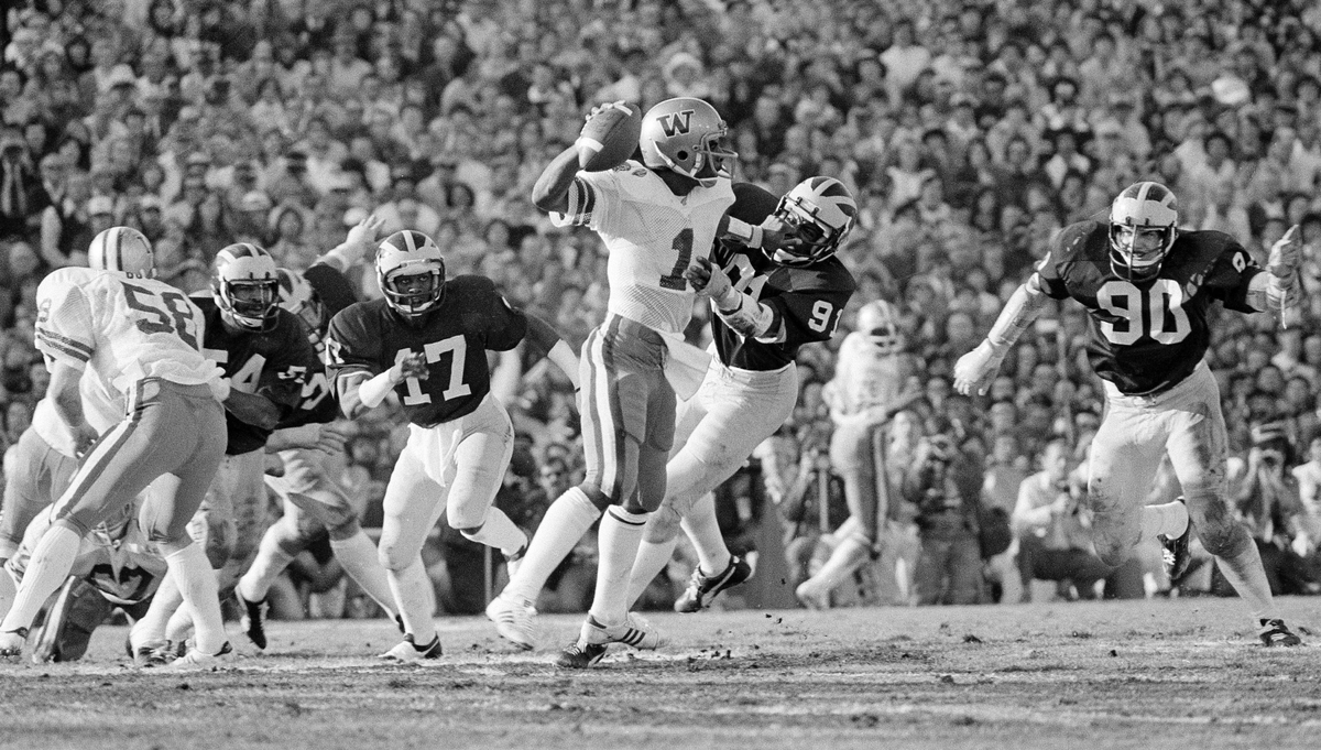 Washington Huskies’ quarterback Warren Moon (1), most valuable player of the Rose Bowl, fends off Michigan Wolverines’ Tom Seabron (91) with a face mask grab as he tries to pass during Rose Bowl action in Pasadena, Jan. 3, 1978.