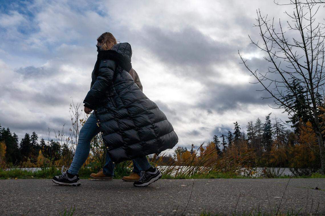A swift gust of wind blows a women’s long coat back as she walks along a path next to Wapato Lake on Sunday afternoon in Tacoma.