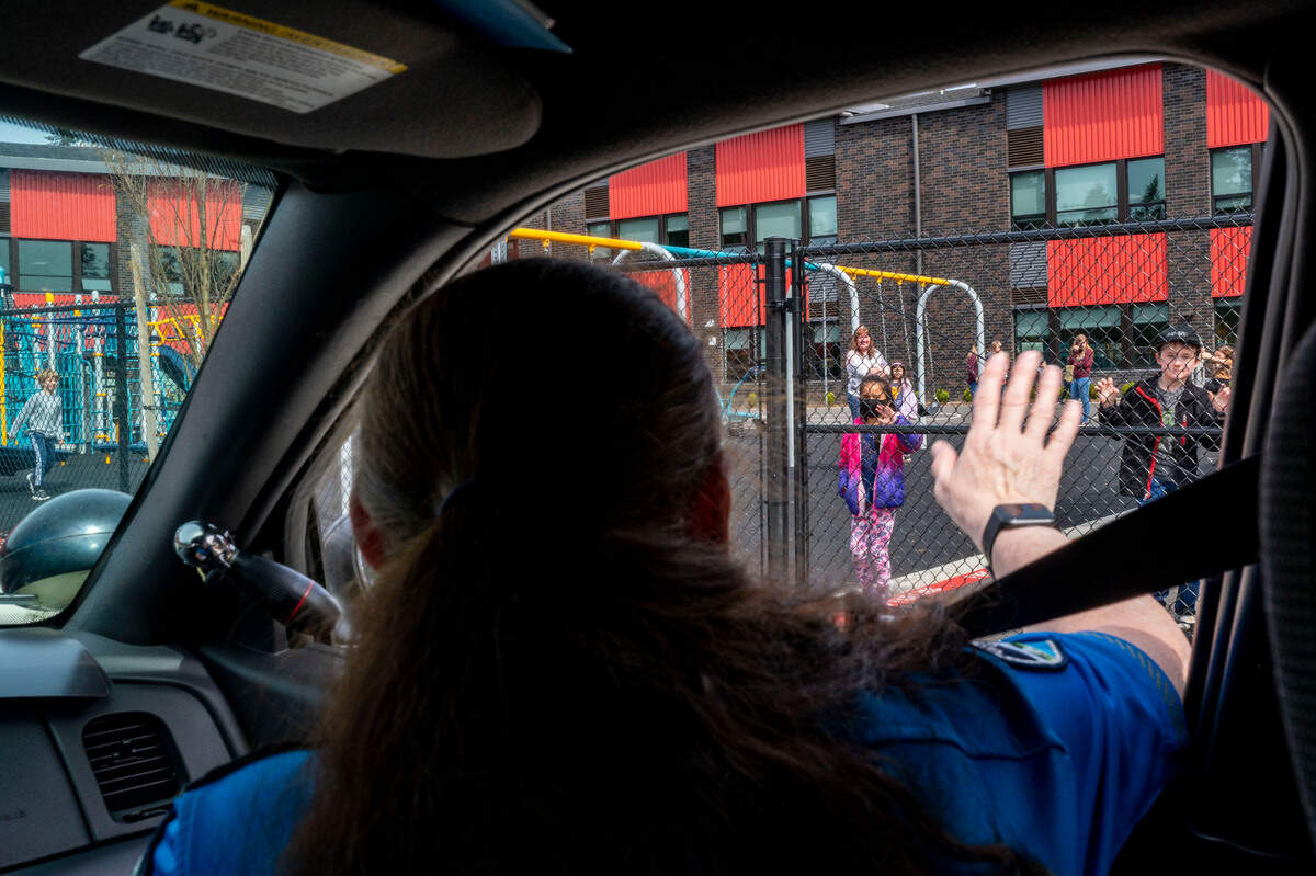 Gig Harbor Police Department volunteer Kim Crowder waves at students at Swift Water Elementary School on Wednesday, April 6, 2022, in Gig Harbor, Wash. Both Crowder and fellow C.O.P.S volunteer Larry Geringer (driving there patrol car), say this is one of the highlights of their day, being able to make a quick and meaningful connection to the young children in the community.