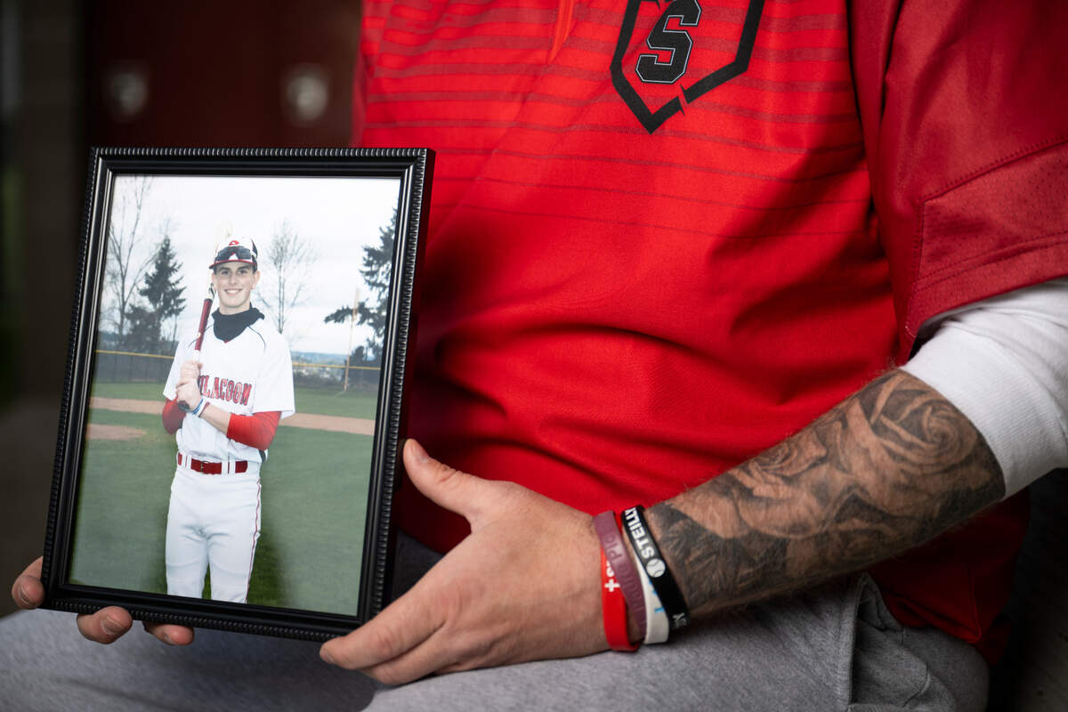 Steilacoom head baseball coach Corey Widman holds a photo of his son Reese Widman, who he lost to suicide last winter, at Steilacoom High School, on Monday, April 15, 2024, in Steilacoom, Wash. The tattoo on Widman’s arm was the exact tattoo Reese was planning to get before his death.
