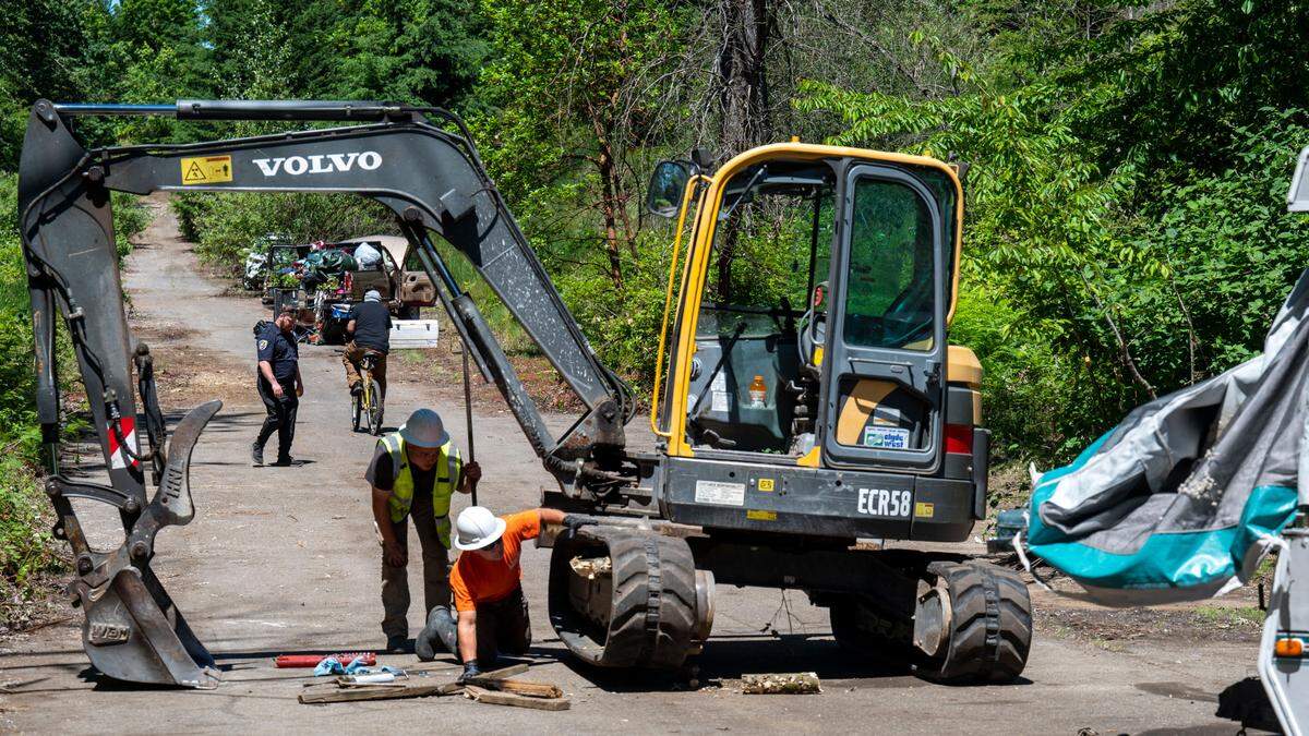 A member of a security guard service (left) walks across a path that led to a homeless encampment near Cheney Stadium on Friday, June 24, 2022, in Tacoma. On Friday, a crew of Metro Parks workers cleaned up a few camps on the land where Pierce County Council candidate Josh Harris shot a man living there at the end of May during an attempt by Harris and other civilians to recover allegedly stolen property.