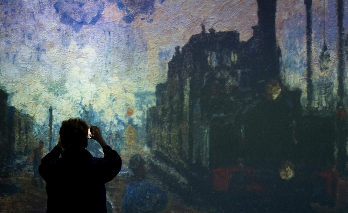 A guest takes a photo of a Monet painting as it is projected onto the walls of the “Imagine Monet” experience at the Tacoma Armory, on Thursday, April 4, 2024, in Tacoma, Wash.