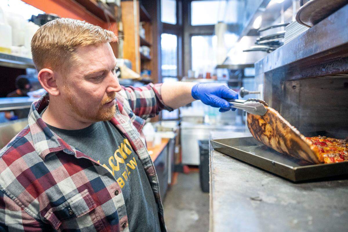 Chef Jacob Thacker checks the bottom of the crust for optimal spotting on one of E9 Firehouse’s new thin-crust pizzas. Cooked in blue steel pans, ideal for pizza-making, the pies are sliced into 12 pieces and served in a standard stainless steel baking sheet.