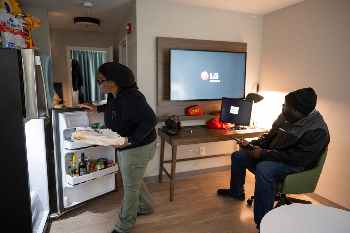 Renee Niles starts preparing dinner as husband Alphonso turns on the television at Staybridge Suites, on Wednesday, Feb. 7, 2024, in Federal Way, Washington. They, their three sons and dog have been living at the hotel for five months after being displaced from their home in Spanaway due to water damage.