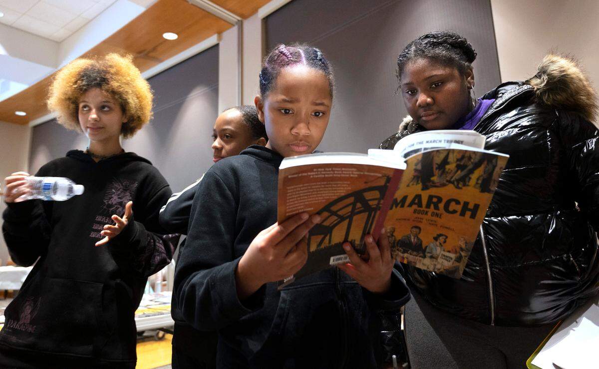 Taina Harrison (center) and Lyric Alexander look over the book “March” during the Young Black & Brilliant book club at the Puyallup Public Library in Puyallup, Washington, on Thursday, Jan. 19, 2023. At left are Len Gardner and Kailee Saunders.