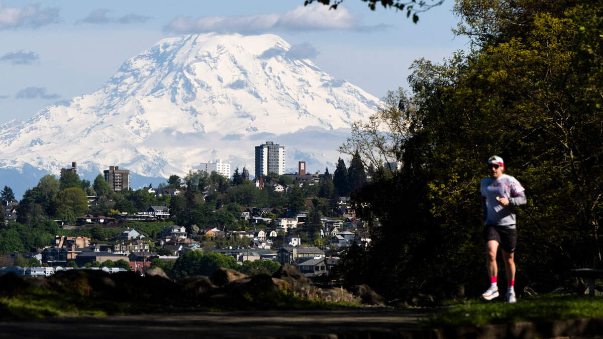 A runner jogs along the Ruston Way trail as Mount Rainier looms through the partly cloudy skies on Wednesday, May 8, 2024, in Tacoma. Weathers forecasters are predicting temperatures into the low 80s this coming weekend.
