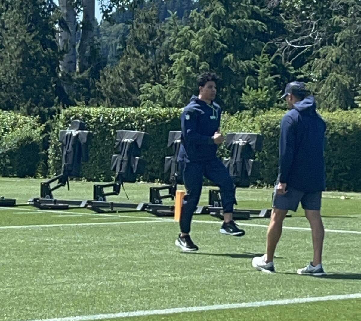 Zach Charbonnet (center, striding) works with a trainer on stepping drills on a side field at the start of practice at Seattle Seahawks NFL mandatory minicamp Tuesday, June 9, 2026, at the Virginia Mason Athletic Center in Renton. It was four months after the running back had surgery to repair a torn anterior cruciate ligament in his knee.