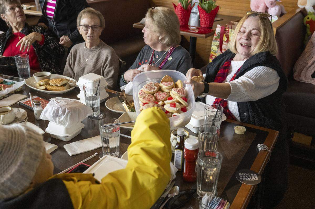 Pam Dean, right, passes a tub of homemade cookies brought by Sue Newman to the Bon crew's monthly lunch on Thursday, Feb. 19, 2026, at the Ram Restaurant in Tacoma, Wash.