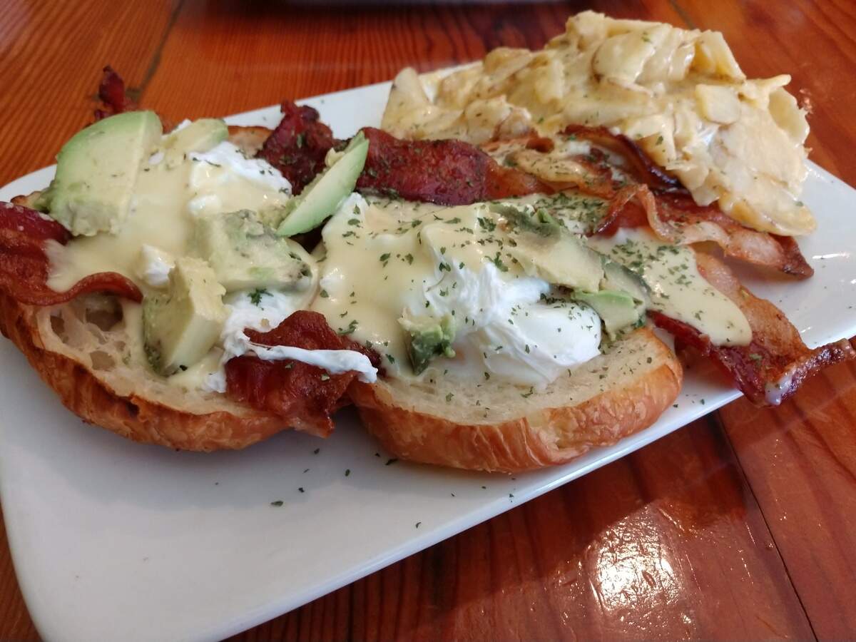 A Benedict with bacon, avocado, hollandaise and poached eggs on a croissant.