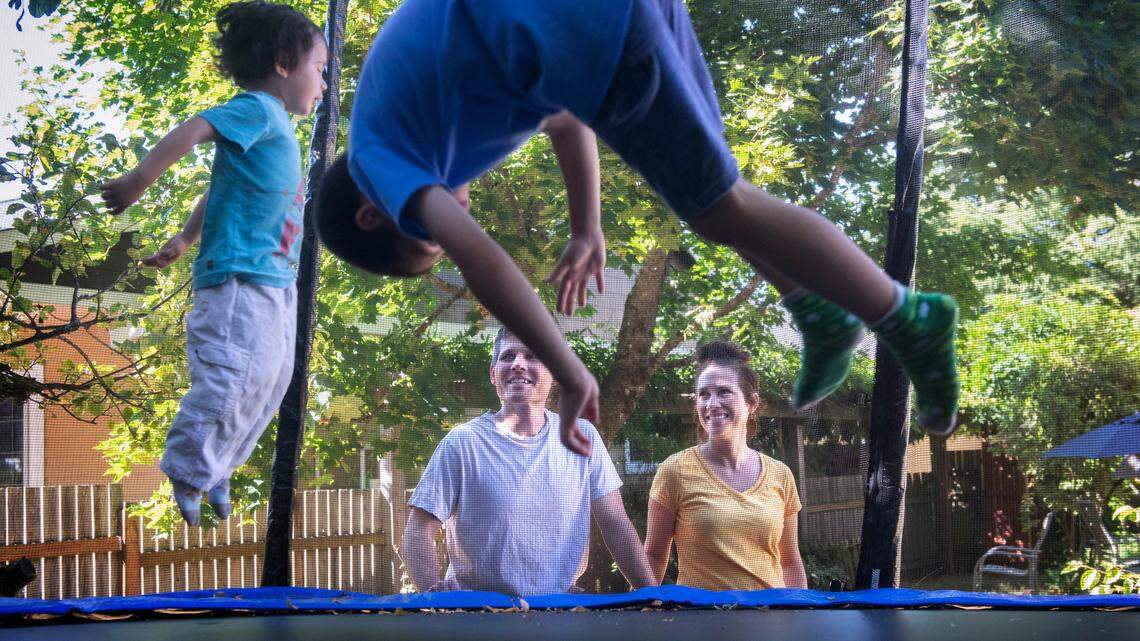Clay Krauss (left) and Juel Lugo watch their boys, Arlo, 3, and Leon, 7, play on the trampoline they bought to keep the kids entertained during the COVID-19 pandemic. The family is shown at their home in Tacoma, Washington, on Wednesday, Aug. 11, 2021.