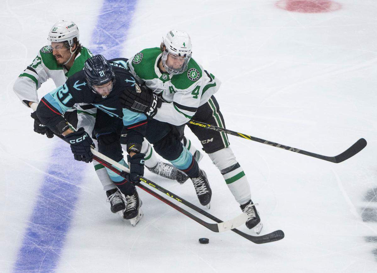 Seattle Kraken center Alex Wennberg (21) tries to keep control of the puck as Dallas Stars left wing Mason Marchment (27) and Dallas Stars defenseman Miro Heiskanen (4) try to shove out of the way during the first period of game four of the second round of the 2023 Stanley Cup Playoffs in Seattle, Wash. on May 9, 2023.