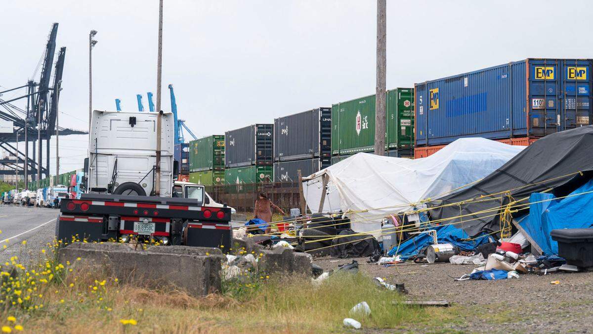 A woman carries belongings to a nearby can at a homeless encampment along Milwaukee Way on Wednesday, June 15, 2022, in Tacoma, Wash. The city of Tacoma says this particular homeless camp along with another one underneath the Murray Morgan Bridge have been the sites of a significant increase in emergency services requests.