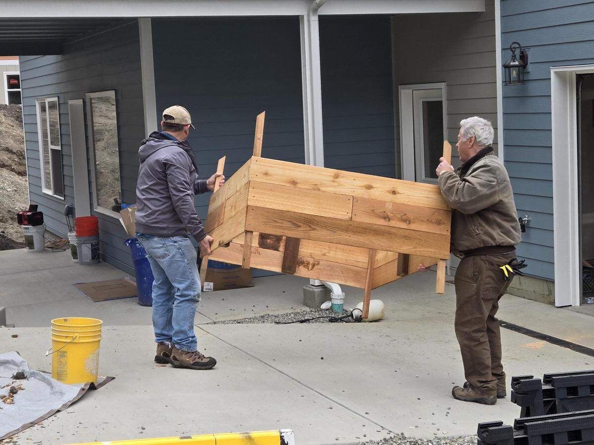 Rich Phillips (right) and David Entzminger carry a garden bed April 6, 2024 at the last work day for the latest Tacoma/Pierce County Habitat For Humanity homes in the Gig Harbor area.