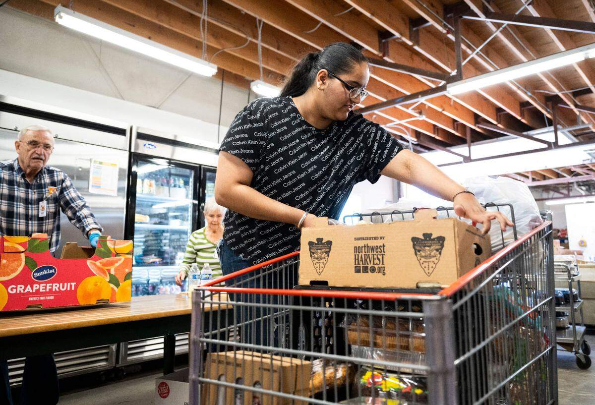 Puyallup High School senior Gurnoor Nagra places a box of food into a shopping cart while delivering meals to families waiting in their cars outside of the Puyallup Food Bank in Puyallup, Wash. on April 27, 2023. Nagra has been volunteering at the food bank for about two years and has dedicated over 400 volunteer hours to helping her community.