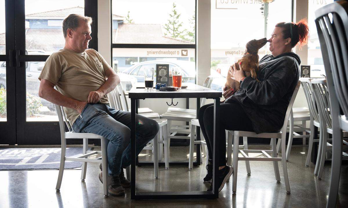 Philip Johnson and Stacy Sasse sit with pup “Henry” at Top Down Brewing Co. in Sumner, Wash. on April 5, 2023. The FDA updated the food code in 2022 to allow dogs, under certain circumstances, at bars and restaurants.