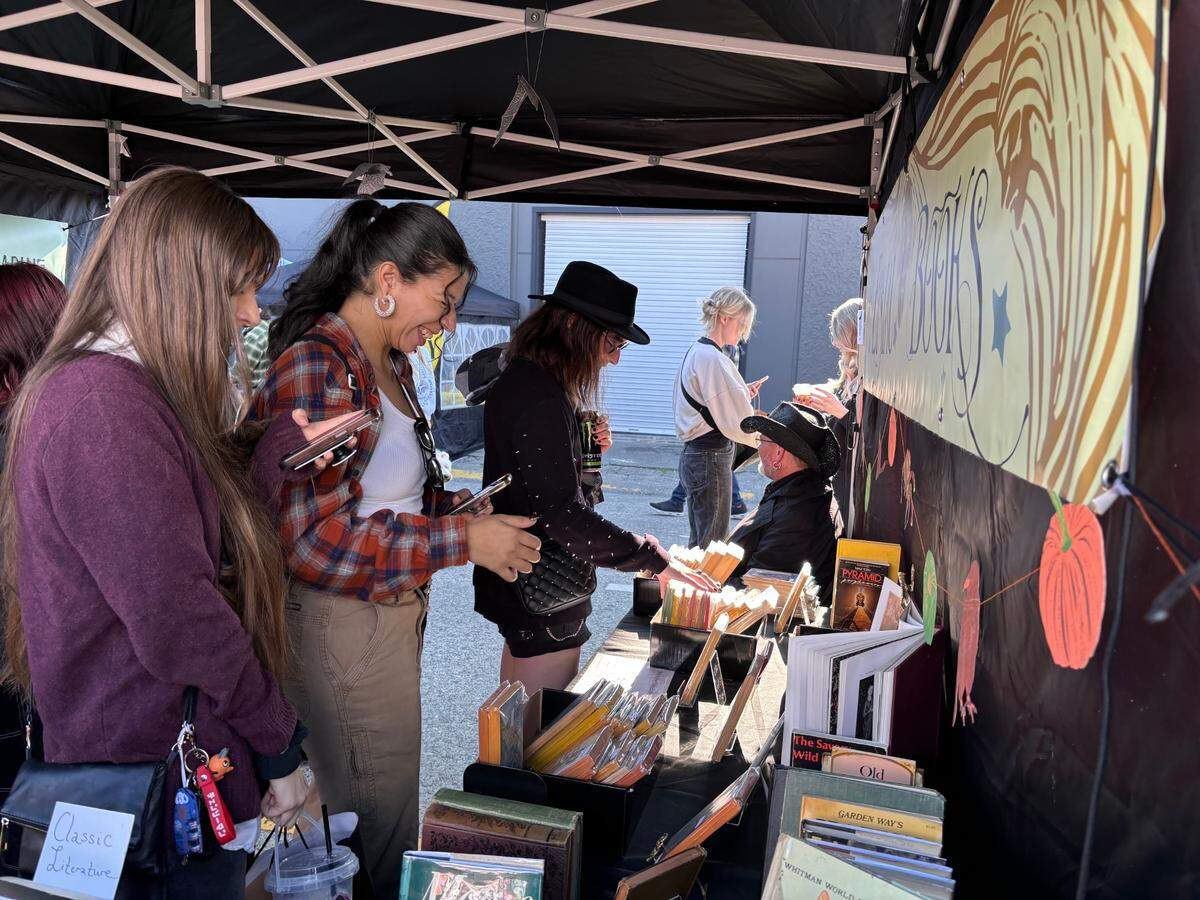 Market-goers look through books and notebooks at the Eisiau Books booth at the Haunted Farmers Market.