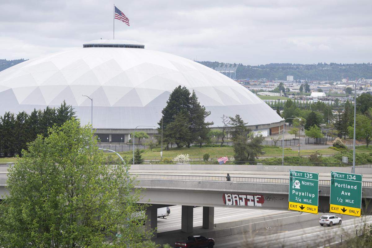 An American flag blows in the wind from the top of the Tacoma Dome as Shaun Anderson stands below on an overpass, waving an upside down American flag to cars moving along Interstate 5, on Wednesday, May 6, 2026, in Tacoma, Wash.