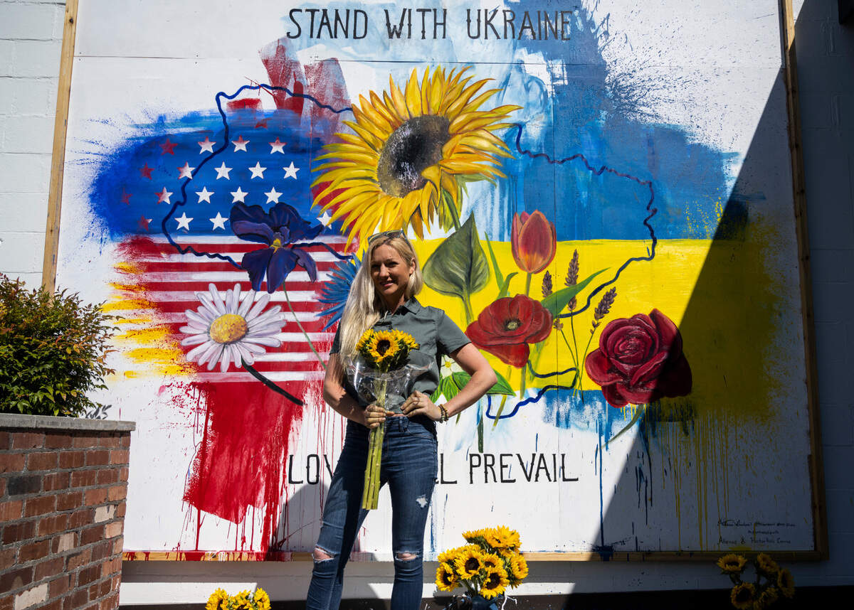 Hillarie Isackson poses for a portrait in front of a mural she painted on the side of her studio in support of Ukraine, in Gig Harbor, Wash. on Friday, April 8, 2022. Isackson’s original mural was vandalized and she spent an entire night recreating a new piece incorporating the vandalism to represent Ukraine and her community’s resilience.