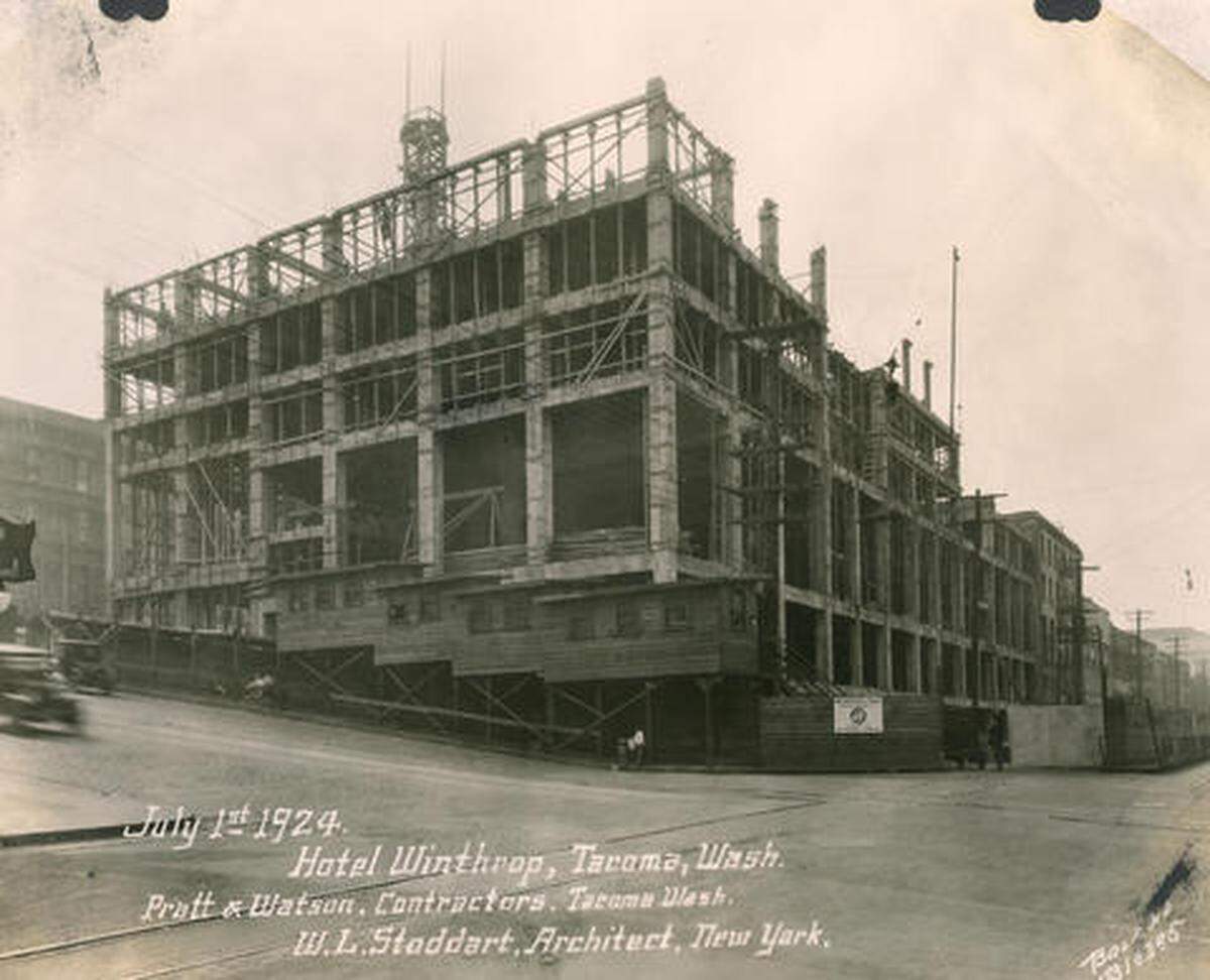 Progress photograph of the construction of the Hotel Winthrop. Work continues on the building of the eleven story hotel by Pratt & Watson contractors in July of 1924. It appears that construction has reached the fourth floor. A notice has already been posted that the stores in the hotel will be under the management of the W.H. Opie & Co.