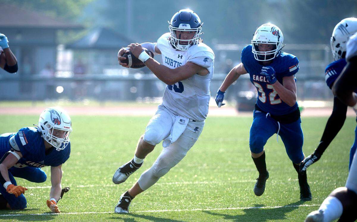Curtis quarterback Rocco Koch scramlbes between Graham-Kapowsin defenders Ethan Pletcher (left) and Josh Massey during Saturday’s football game at Art Crate Field in Spanaway, Washington, Oct. 8, 2022. Graham-Kapowsin won the game, 24-19.