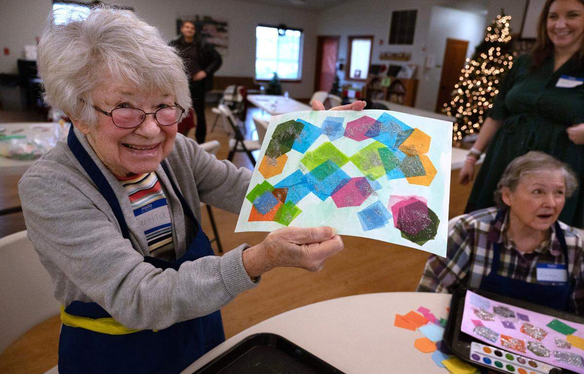Martha Schumacher shows off her finished artwork during the Lutheran Community Services’ Opening Minds Through Art program at the Mountain View Community Center in Edgewood, Washington, on Wednesday, Dec. 6, 2023.