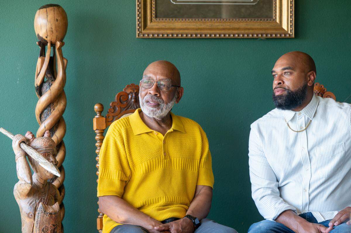 Father and son, Leon Walker, left, and Rob Young, sit together in Walker’s home on Monday, June 9, 2025, in Tacoma, Wash. African art, including a wooden warrior sculpture from Ghana, front, and an ebony sculpture by a Benin artist from Walker’s former art gallery, decorates the home.