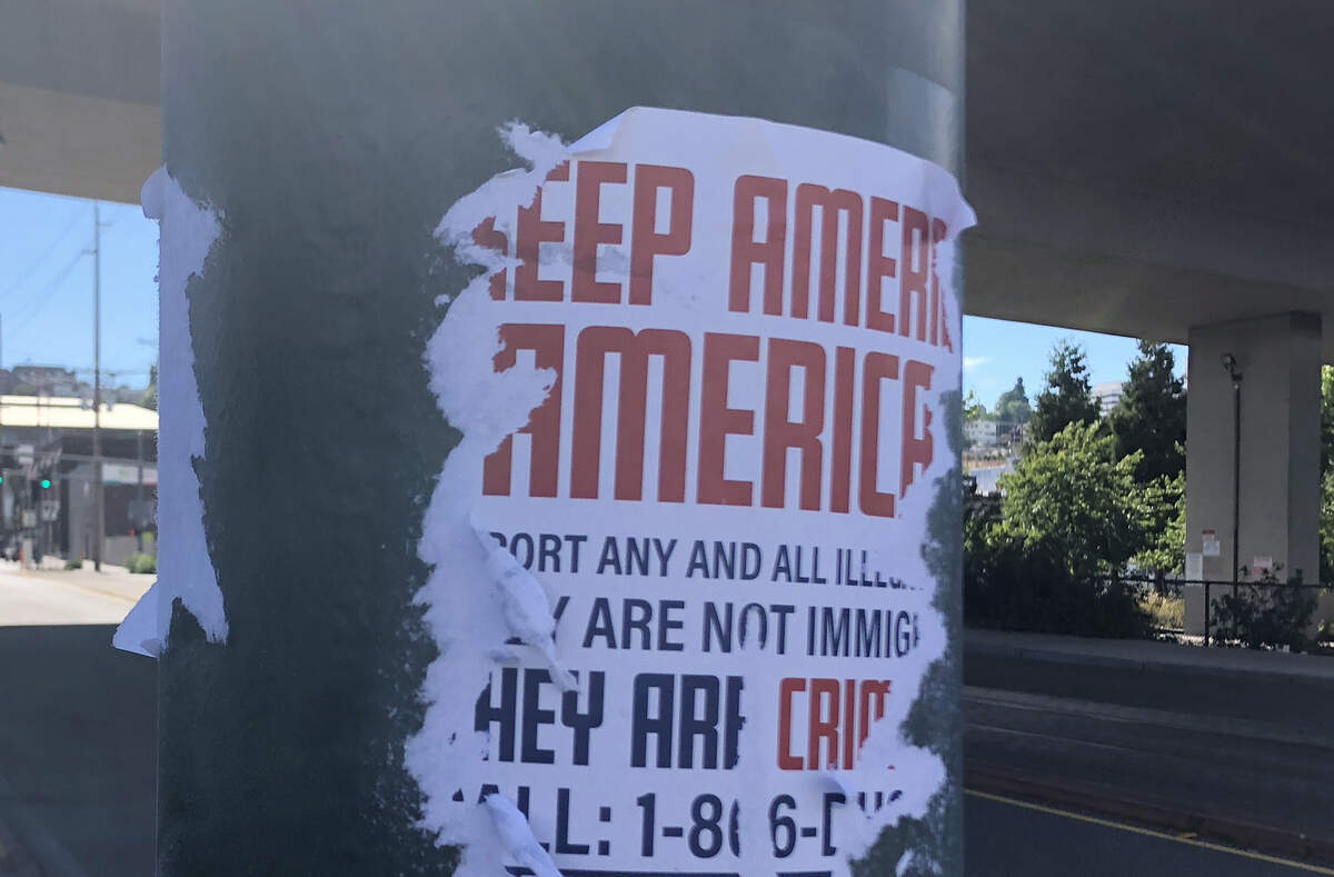 A poster produced by a white supremacist group is glued to a Tacoma city utility pole at South 25th and A Streets Sunday. It had already been partially torn down before being scrubbed off by Halley Knigge.