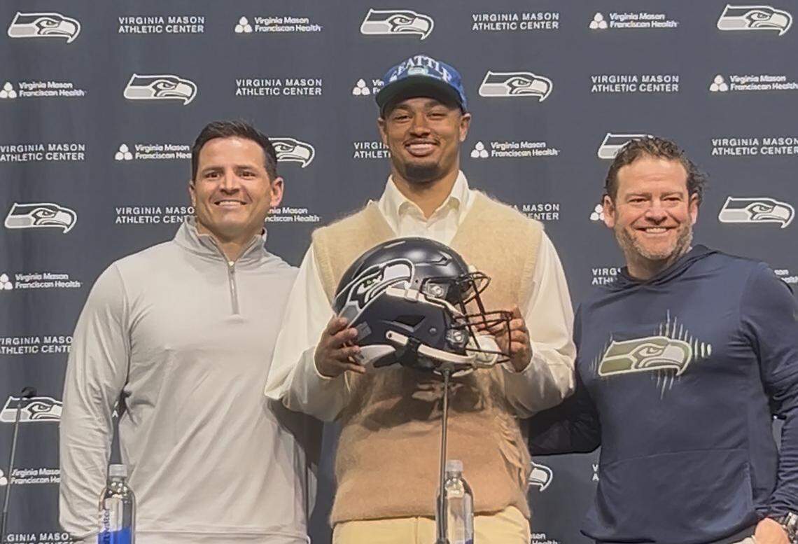 All-Pro wide receiver Jaxon Smith-Njigba, NFL offensive player of the year for 2025, flanked by coach Mike Macdonald (left) and general manager John Schneider (right) after signing his four-year contract extension with the Seattle Seahawks Wednesday, March 25, 2026, at the team’s Virginia Mason Athletic Center in Renton.