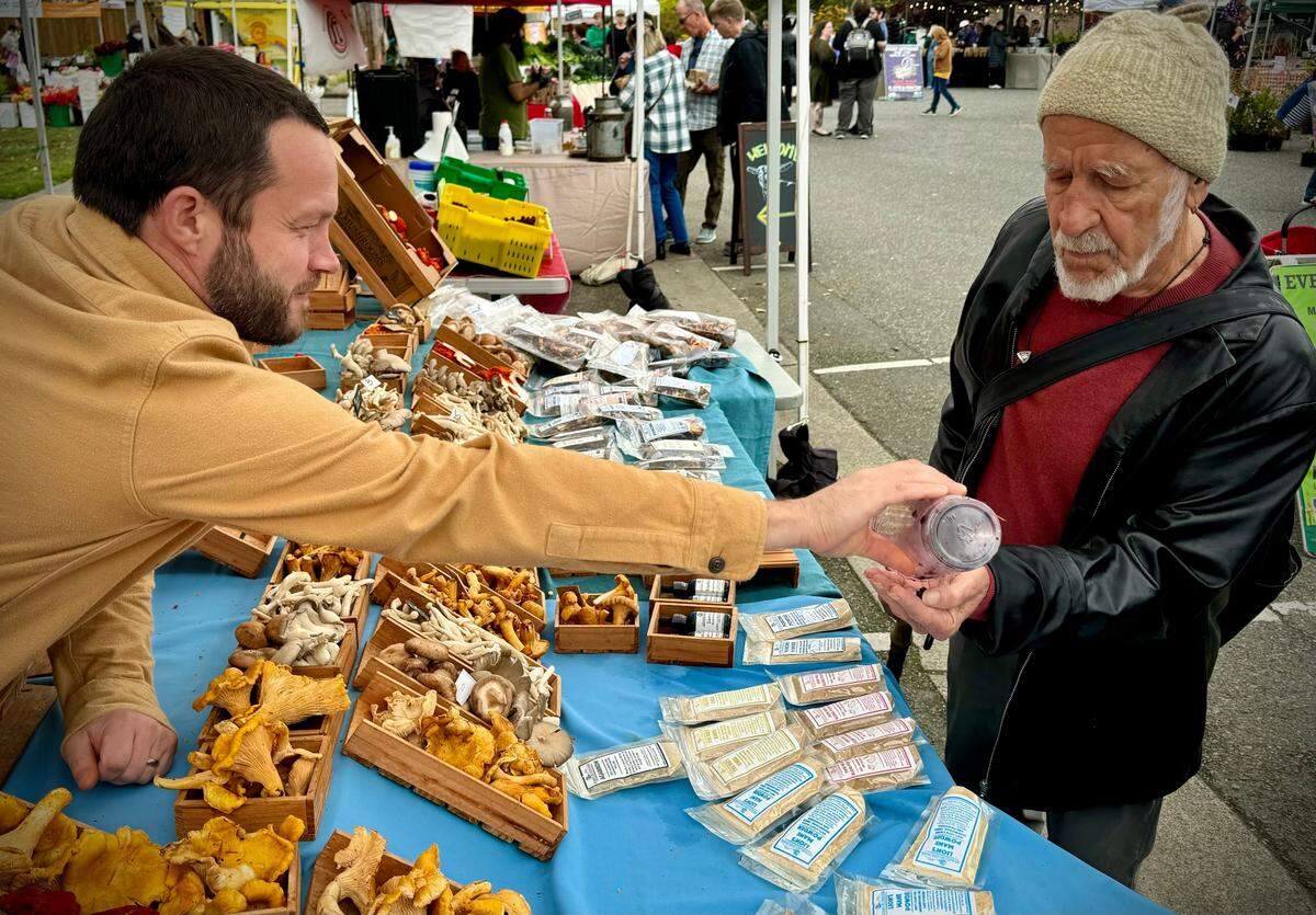 Adam DeLeo, owner of Adam’s Mushrooms, hands a sample of wild huckleberries to Gordon Barnett of Tacoma at the Proctor Farmers Market on Saturday, Oct. 19, 2024.