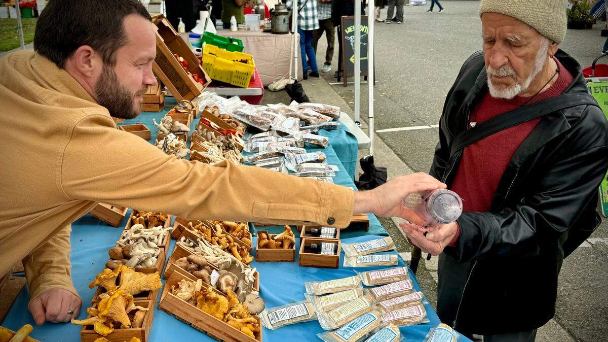 Adam DeLeo, owner of Adam’s Mushrooms, hands a sample of wild huckleberries to Gordon Barnett of Tacoma at the Proctor Farmers Market on Saturday, Oct. 19, 2024.