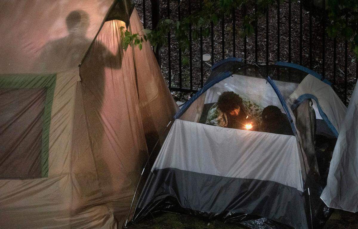 Three men prepare to smoke from a glass pipe at a homeless encampment along 82nd Street between the Best Western Plus and Hampton Inn & Suites on Hosmer Street in Tacoma, Washington on June 28, 2022.