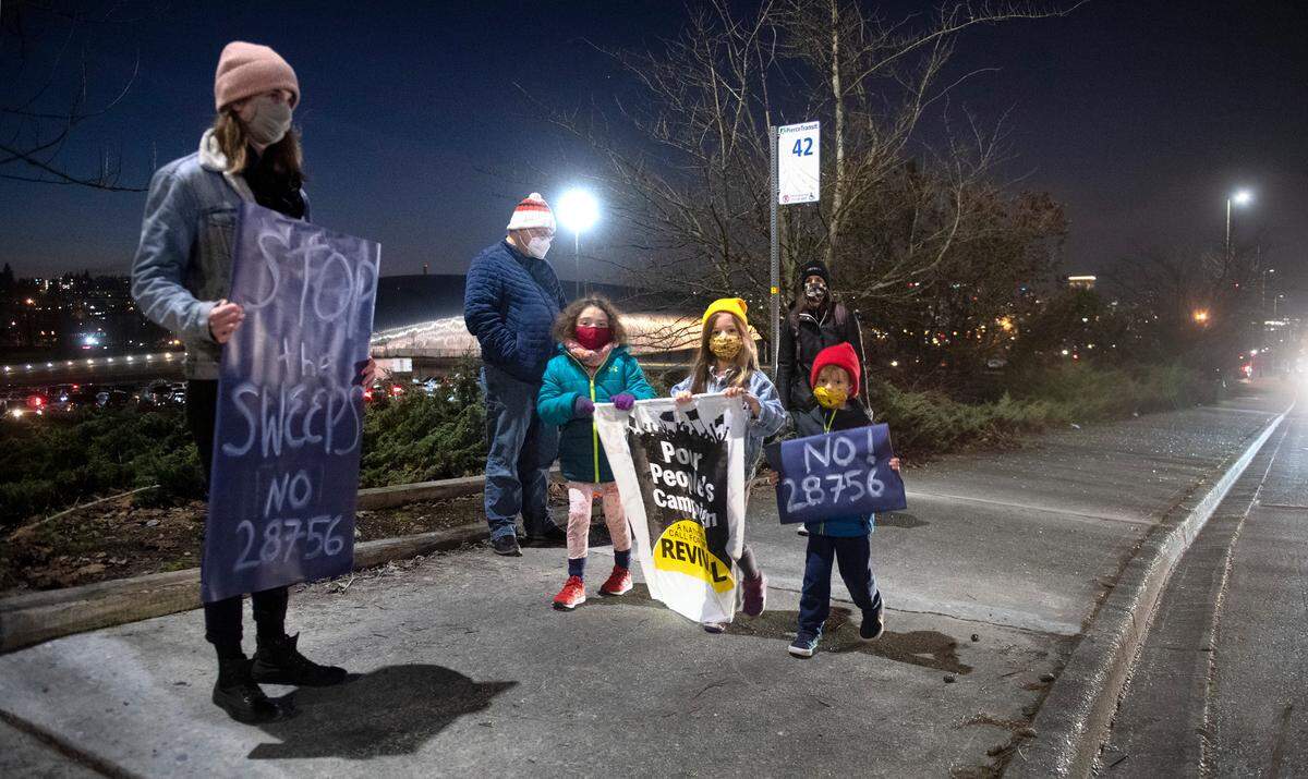 Jamie Fiano of Tacoma holds a sign as Drew Galazin, 6, Luella Petersen, 6, and Leo Peterson, 5, march past during a demonstration outside the Tacoma Safe meeting at the LeMay - America’s Car Museum in Tacoma, on Wednesday, Jan. 26, 2022.