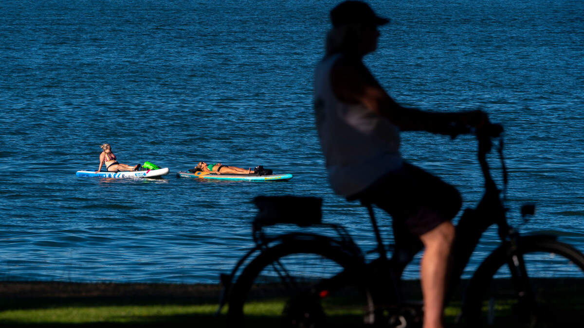 Paddle boarders take a break in Commencement Bay as a cyclist rides along the Ruston Way Path on Tuesday, July 19, 2022, in Tacoma, Wash. Temperatures are forecasted to reach into the 90s this week as people find any way possible to stay cool during the heat wave.
