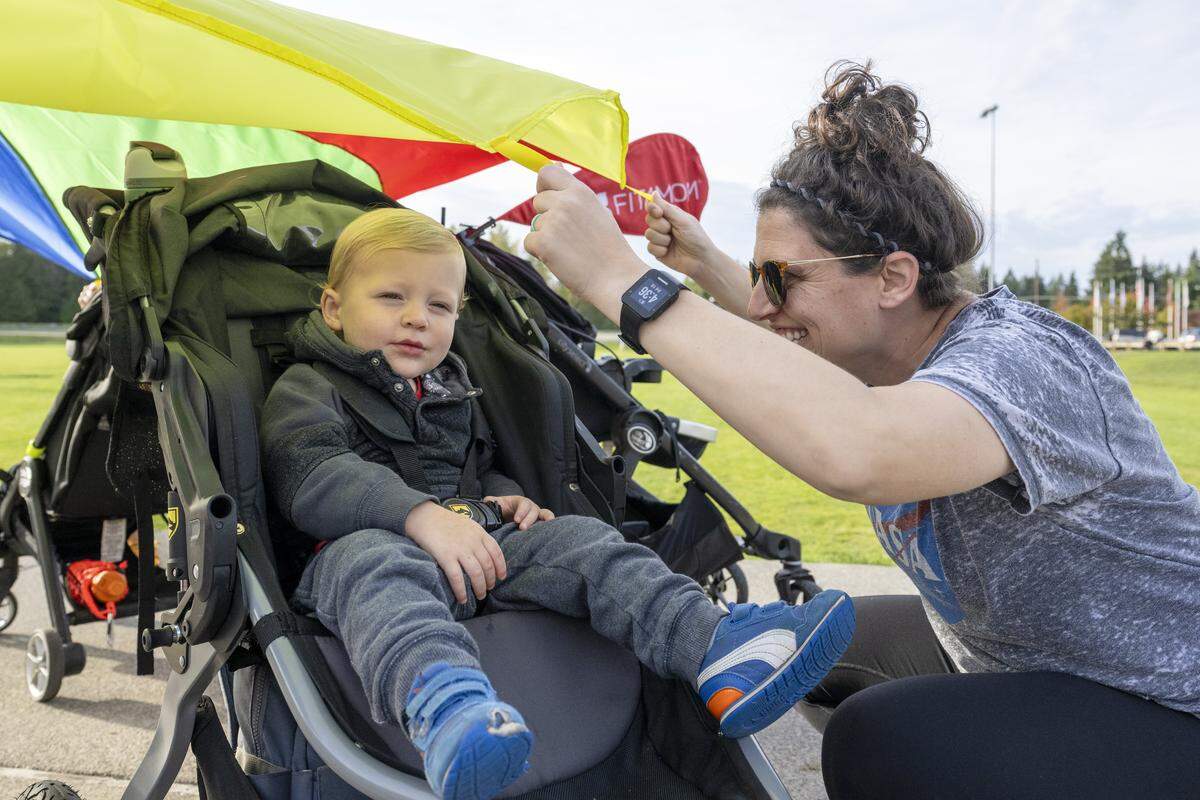 Reed, 1, smiles as mom Tara Rohrbough, right, drops a parachute over him as part of an ab exercise with Fit4Mom University Place on Thursday, Oct. 9, 2025, at Cirque Park in University Place, Wash.