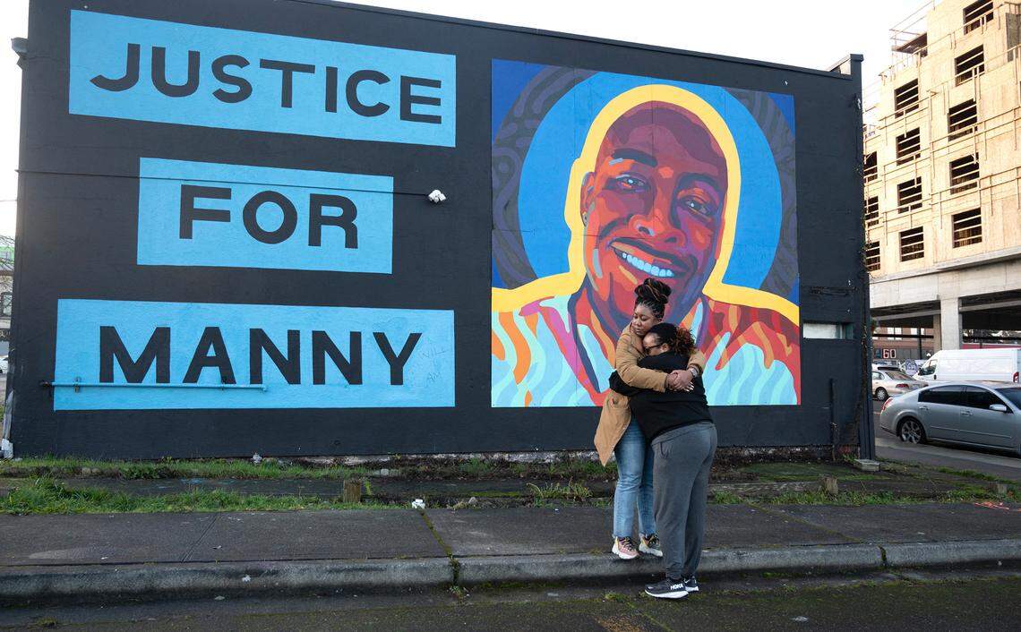 Monet Carter-Mixon (facing away) and a woman who asked to not be identified hug in front of the mural for Carter-Mixon’s brother, Manny Ellis, in Tacoma on Thursday, Dec. 21, 2023, following the not-guilty verdicts for three Tacoma police officers criminally charged in his death.
