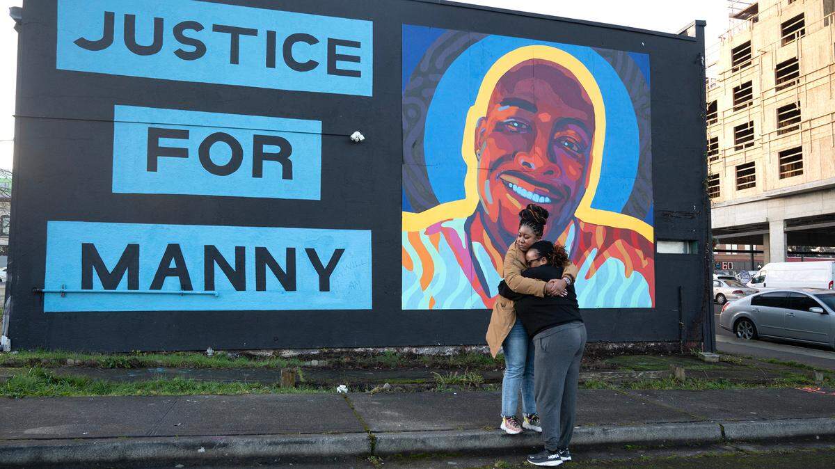 Monet Carter-Mixon (facing away) and a woman who asked ot not be identified hug in front of the mural for Carter-Mixon’s brother, Manny Ellis, in Tacoma, Wash., on Thursday, Dec. 21, 2023, following the not guilty verdicts for all three Tacoma police officers criminally charged in his death.