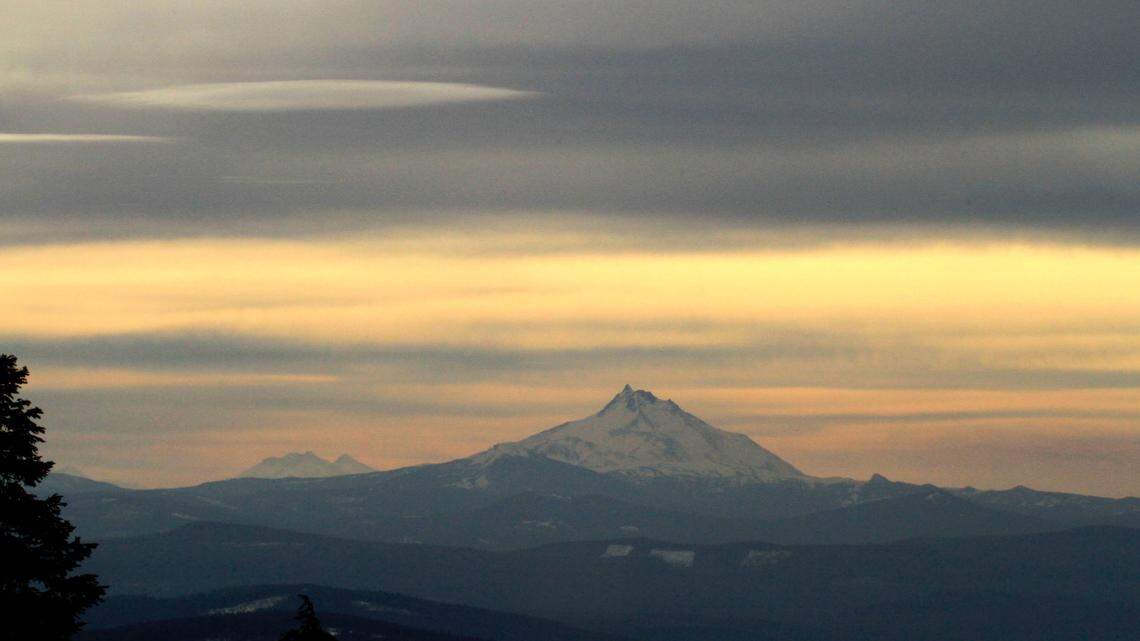A hazy, brownish layer hovers under clouds around Oregon’s Mount Jefferson as seen from Mount Hood near Government Camp, Ore., in 2011. A search continues for a 33-year-old hiker who was last seen plunging hundreds of feet Friday in treacherous terrain on Mount Jefferson.