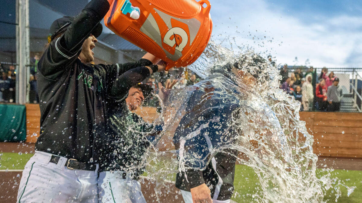 Auburn’s Tanner Hanson (left) and Colton Anardi douse head coach Gordie Elliott with water after beating Peninsula, 3-1, to win the 3A District 3/4 championship game on Saturday, May 14, 2022, at Auburn High School in Auburn, Wash.