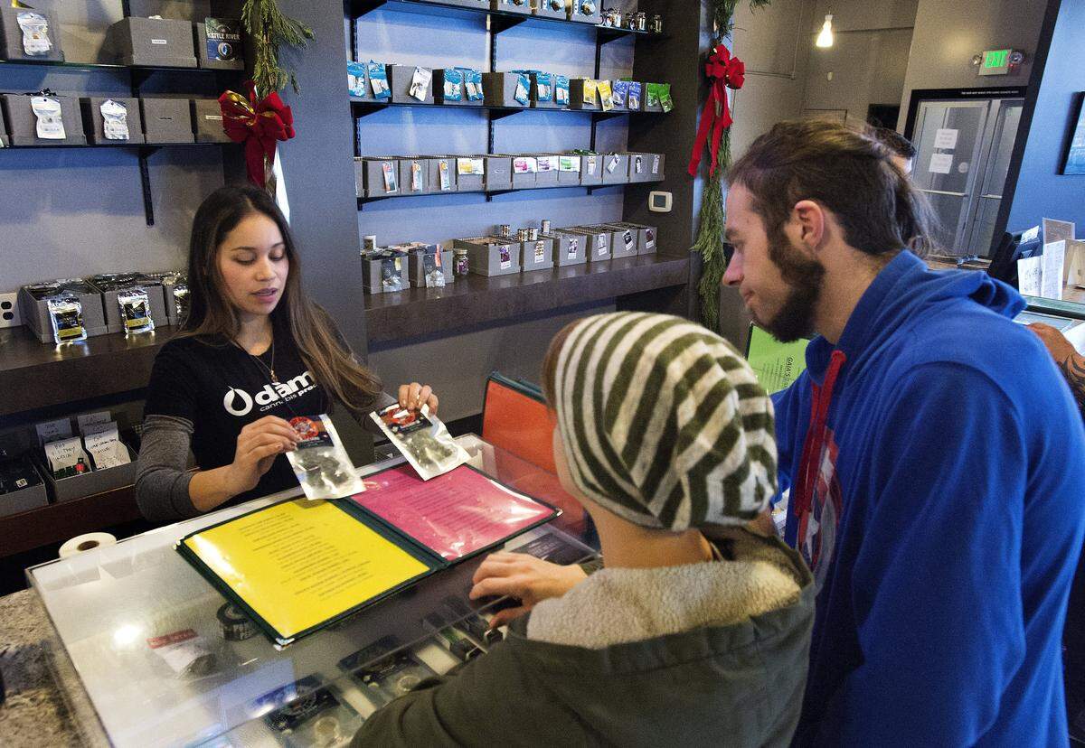 Karen Siu, a budtender with Emerald Leaves, displays two varieties of marijuana to customers Kayla Dearborn and Levi Henderson, in Tacoma on Jan. 5, 2016. 