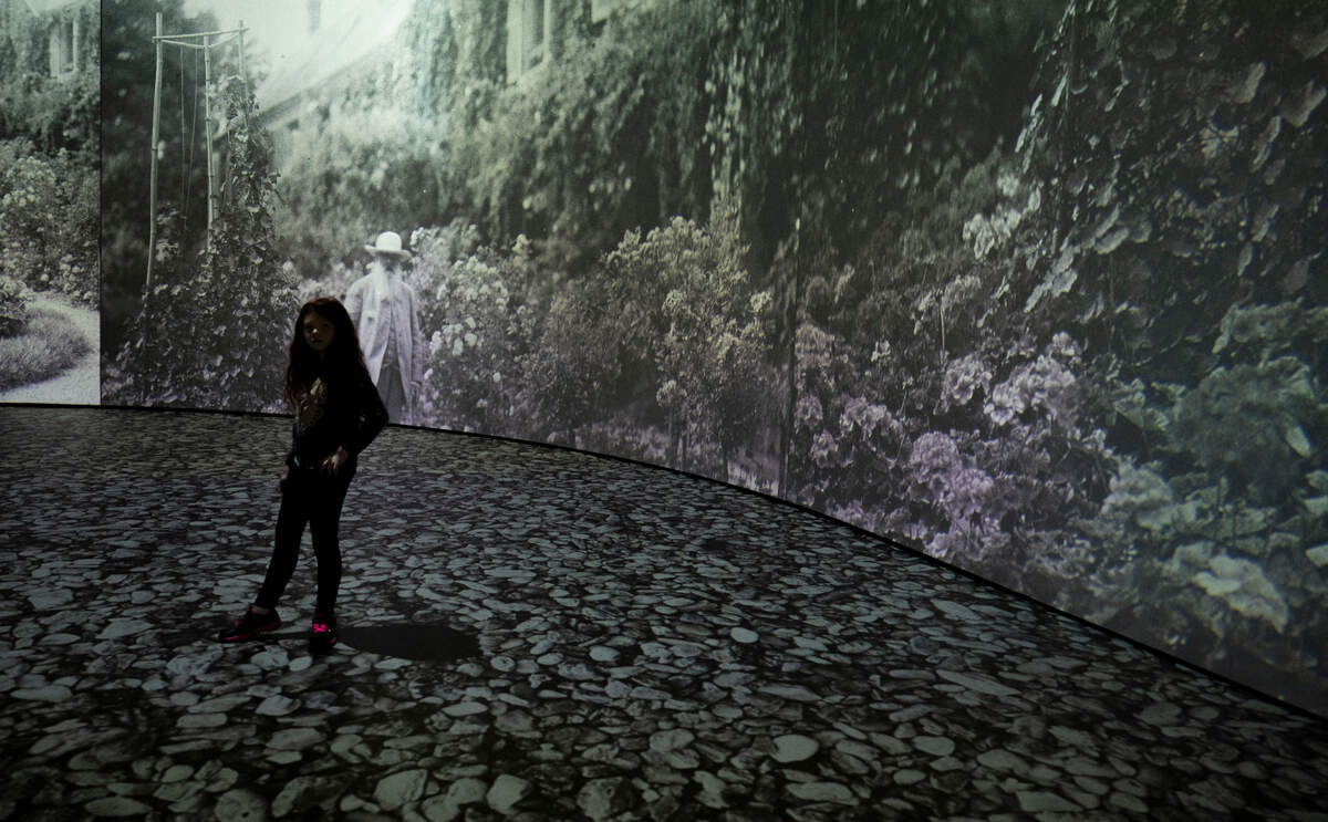 Guests watch as Monet’s painting are projected onto the walls of the “Imagine Monet” experience at the Tacoma Armory, on Thursday, April 4, 2024, in Tacoma, Wash.