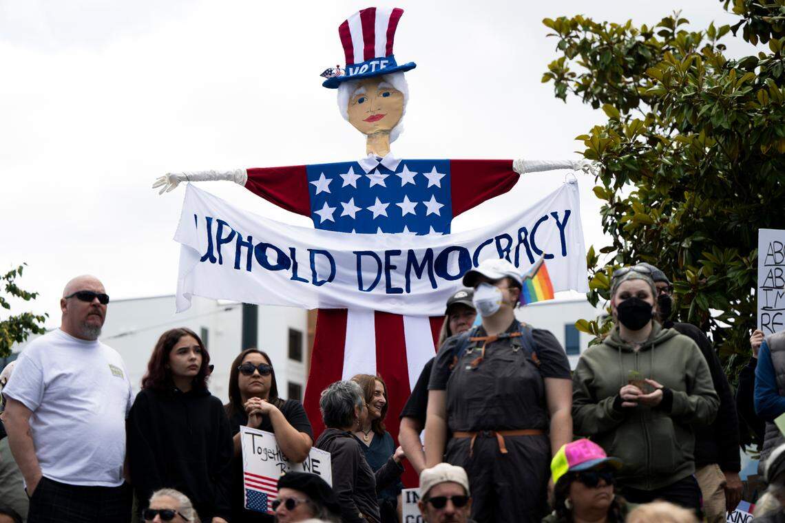 People sit and listen to speakers during a “No Kings” protest at People’s Park on Saturday, June 14, 2025, in Tacoma, Wash.