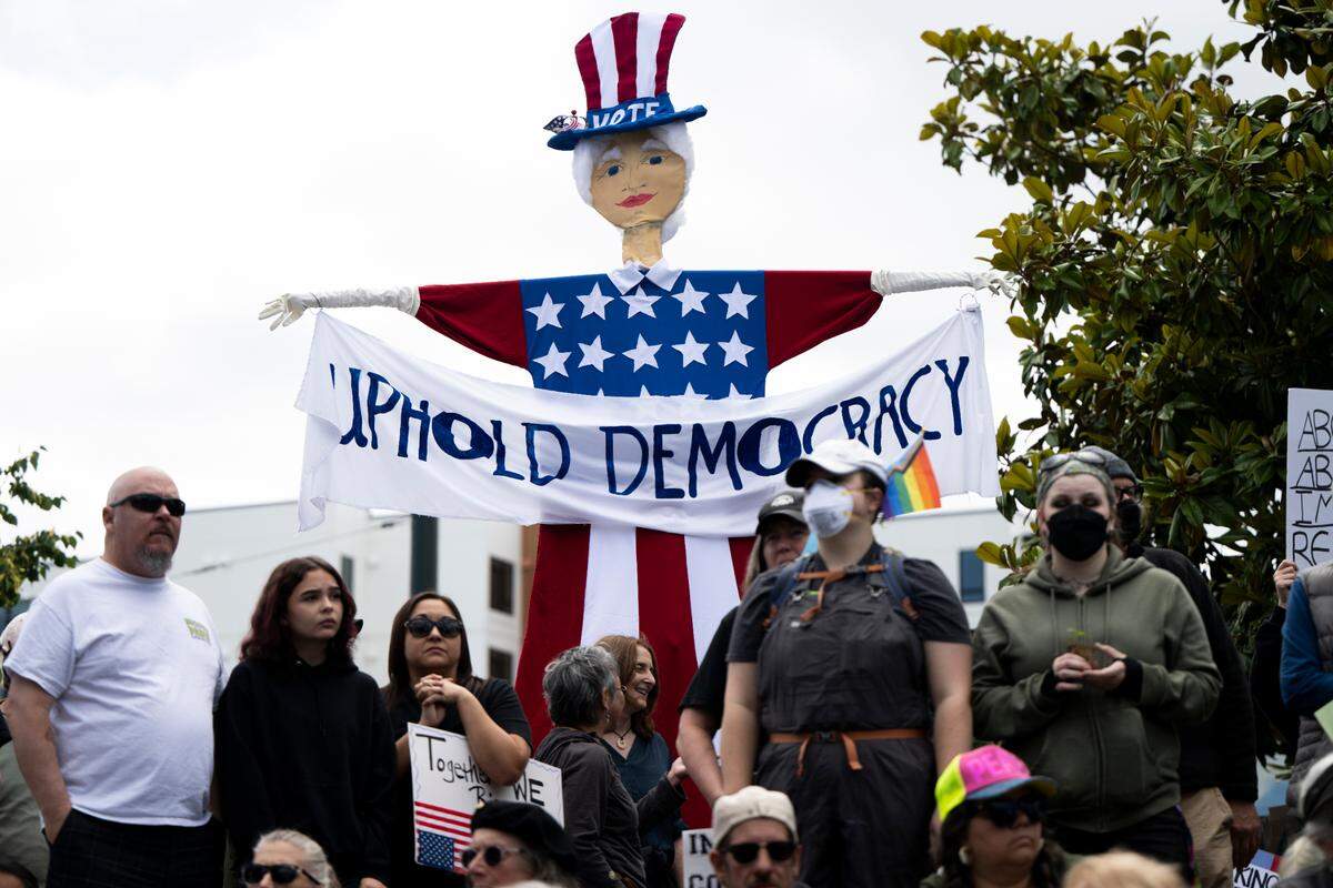 People sit and listen to speakers during a “No Kings” protest at People’s Park on Saturday, June 14, 2025, in Tacoma, Wash.