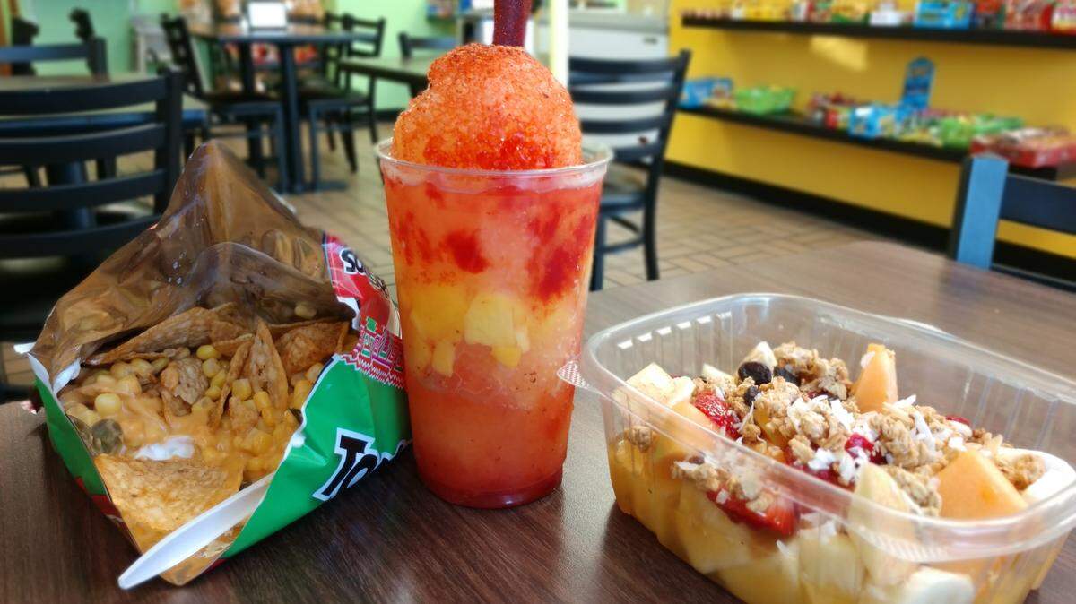 Snacks from La Casa de Sharon in Lakewood. On the left is a bag of Tostielotes, in the middle is a mango raspado and on the right is a container of fresh-cut fruit.
