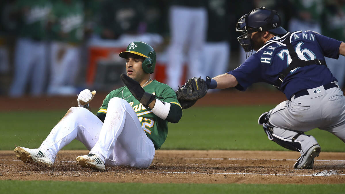 Oakland Athletics’ Ramon Laureano, left, scores past Seattle Mariners catcher Chris Herrmann (26) during the first inning of a baseball game Friday, Aug. 31, 2018, in Oakland, Calif. (AP Photo/Ben Margot)