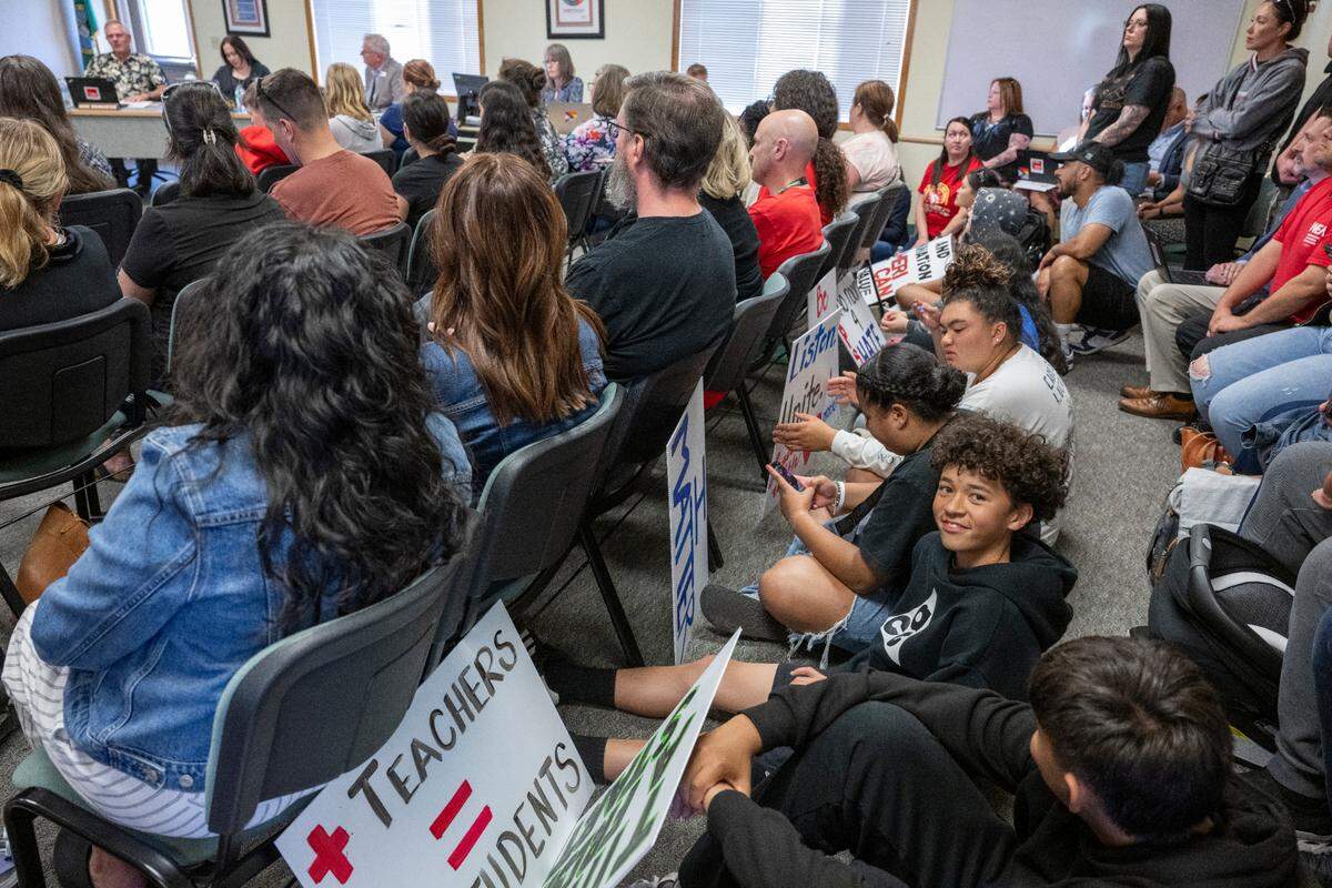 Signs calling attention to discrimination and budgetary cuts are laid against chairs as people sit on the ground of the board room for a Franklin Pierce School District school board meeting on Tuesday, June 3, 2025, at the district’s administrative center in Pierce County. More people stood near the entrance and sat in an overflow room.
