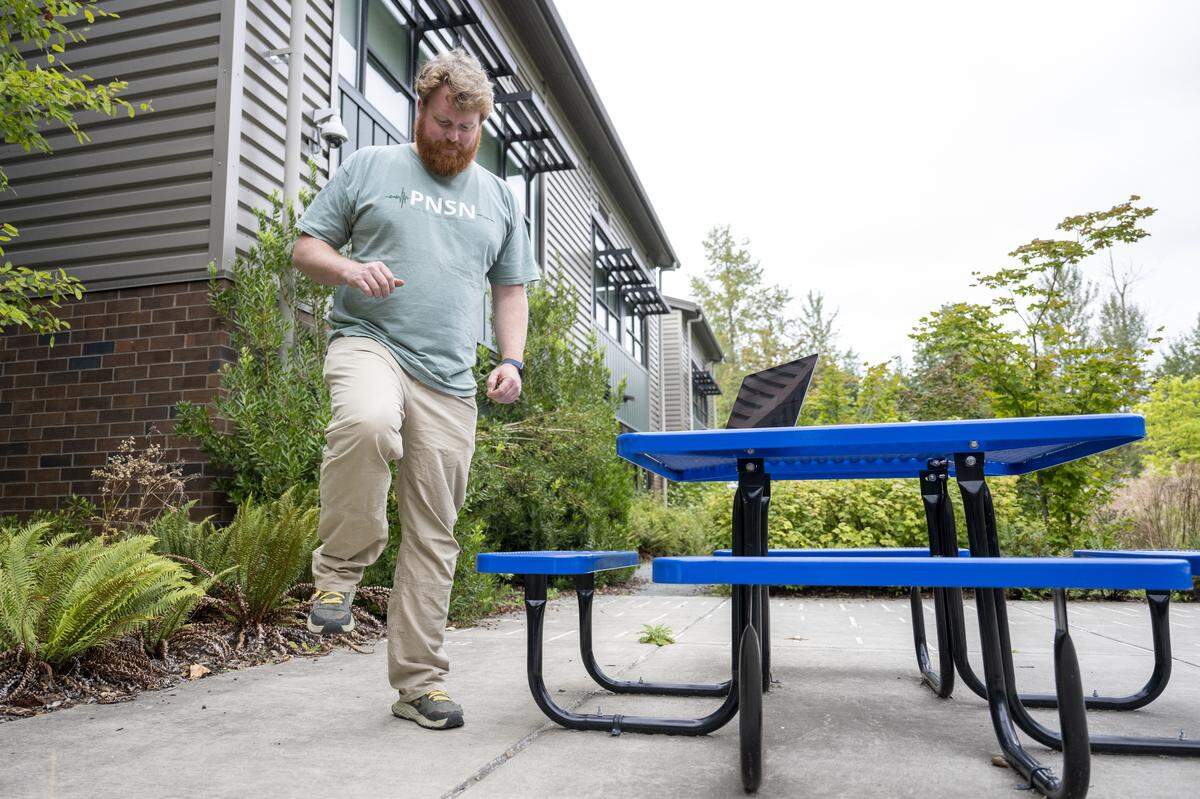 Doug Gibbons, a field technician and seismology lab coordinator for the Pacific Northwest Seismic Network, raises his foot to perform a stomp test in Tehaleh Heights Elementary’s courtyard on Thursday, Sept. 11, 2025, in Bonney Lake. That is where one of the organization’s urban stations is located, and the stomping enables researchers and onlookers to see how movement is recorded in real time online.