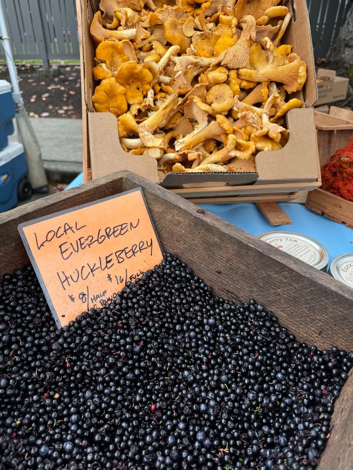 A crate of huckleberries and another of chanterelles beckons shoppers at the Adam’s Mushrooms stand at Tacoma’s Proctor Farmers Market on Saturday, Oct. 19, 2024. Both are wild foraged.