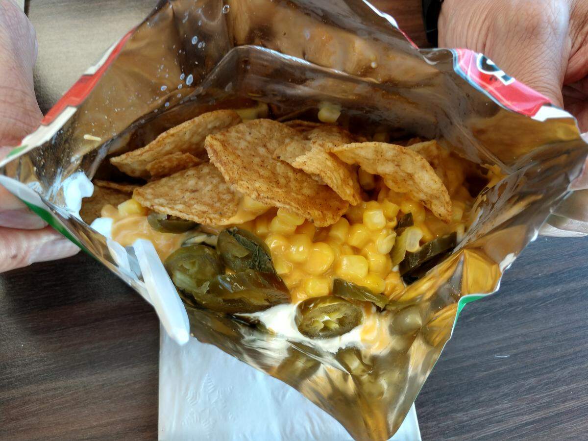 A bag of tostielotes from La Casa de Sharon in Lakewood. Nacho cheese is drizzled into a torn open bag of Tostitos chips and then a handful of pickled jalapenos and corn are thrown in.
